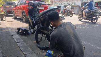 A man repairs a flat tire on a motorcycle on the side of a street in a busy urban area. photo