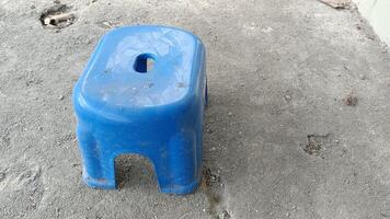 A blue plastic stool sits on a rough concrete surface. photo