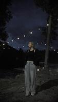 Woman yawning under string lights in a dark forest setting video