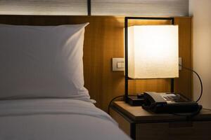 Modern Japanese style bedroom headboard with bed and pillows for sleeping and resting in a dim atmosphere with a bedside light on. Accommodation, hotel. photo