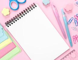 Flatlay composition with blank notepad and school stationery on a pink background. Back to school. Top view. Copy space. photo