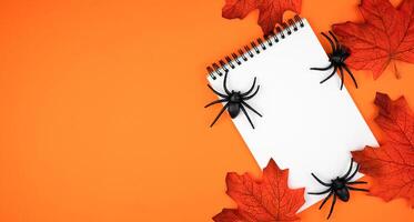 Blank notepad, spiders and autumn leaves on orange background. Composition for Halloween. Flatlay. Top view. Copy space. photo