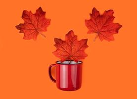 Bright autumn composition with red mug and orange autumn leaves on the orange background. Flatlay. Top view. Selective focus. photo