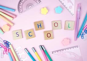 The letters Schooland school stationery lie on a pink background in the form of a frame. Top view. Back to school. photo