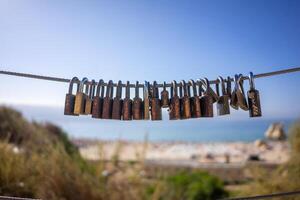 Various padlocks attached to a wire fence with a beach in the background, symbolizing love and commitment. photo
