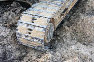 Close-up of excavator caterpillars on rough terrain, showcasing detailed treads and dirt accumulation. Ideal for construction and machinery themes. photo