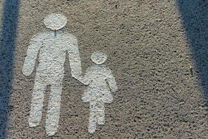 A painted ground image showing a man holding hands with a child, symbolizing a pedestrian walkway. The simple figures, in white, indicate safe crossing for pedestrians. photo