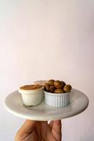 A waiter holds a white plate with green olives, farinheira pate, and surimi pate, ready to serve in a rustic dining setting. photo