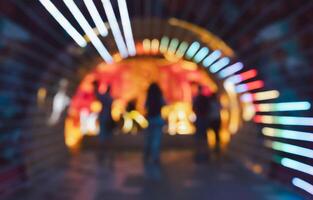 Abstract blurred background of people walking through tunnel illuminated with colorful neon lights photo