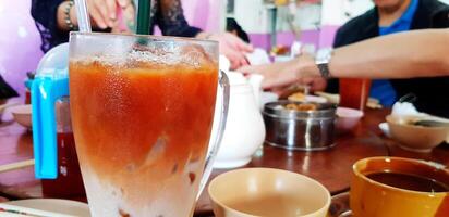 Close up glass of cold milk tea with people eating food for background in Dim sum, Chinese restaurant. Refreshment drink, Food, Sweet drinking and Breakfast time concept photo