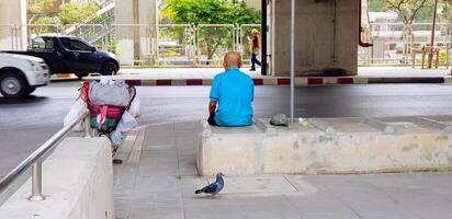 Man sitting on cement or concrete bench and waiting for someone beside bicycle and pigeon walking on the back with car movement and street for background. Lonely person, Transportation and Street life photo