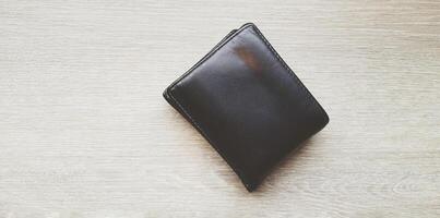 Black or brown leather wallet on light brown wooden table or background with copy space. Object, Money and Shape concept. photo