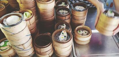 Many kind of hot Dim Sum in weave bamboo basket on stainless steel table for sale and movement of hand taking food for serving customer in Chinese restaurant. Focus on Food and Service concept. photo