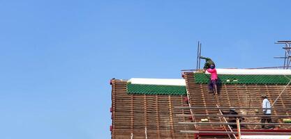 Construction workers repairing or fixing roof of ancient temple and clear blue sky background with copy space at Wat Phra Sri Rattana Mahatat Woramahawihan or Wat Yai temple in Phitsanulok, Thailand. photo