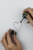 female hands draw a heart with a brush for green nail polish photo