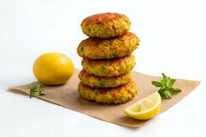 Stack of perfectly fried falafel balls on rustic brown parchment paper, isolated on a white background, with a wedge of lemon and fresh mint for added color and freshness photo