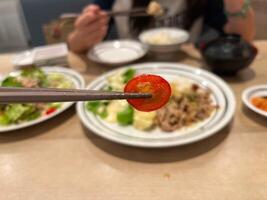 a chopstick is holding a slice of tomato with a blurred background of a meal, capturing the essence of a balanced and nutritious dining experience, Japanese meal photo