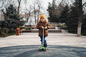 child preschooler kid boy rides a scooter in park on the playground in autumn photo
