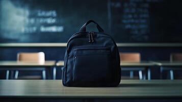 A black backpack sits on a wooden desk in an empty classroom with a chalkboard in the background. photo