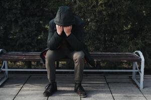 sad lonely man homeless depressed and upset sits on park bench and covers his face with his hands photo
