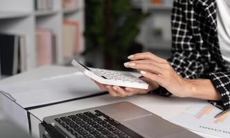 Office Worker Handling Paperwork and Using Calculator at Desk in Modern Workspace with Laptop and Documents photo