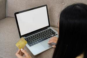 Young Woman Using Credit Card for Online Shopping on Laptop While Sitting on Couch at Home photo