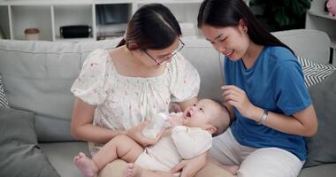 Footage of handheld shot, Happy family having fun with little son while bottle-feed on sofa in the living room, enjoying fun time together. Multi-generation family video