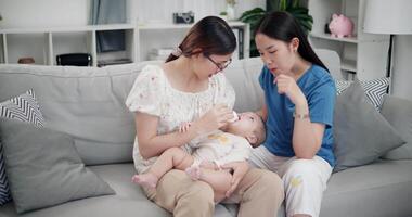 Footage of handheld shot, Happy family having fun with little son while bottle-feed on sofa in the living room, enjoying fun time together. Multi-generation family video