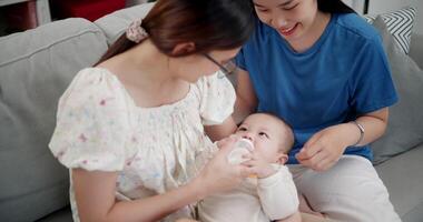 Handheld high angle view shot, Happy family having fun with little son while bottle-feed on sofa in the living room, enjoying fun time together. Multi-generation family video