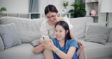 Footage of handheld shot, Two happy women are enjoying watching something together on mobile phones in living room at home. Happy family time ,Having fun on weekend video