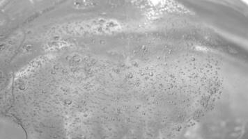 Thin trickle of transparent cosmetic gel with tiny bubbles flows down to the surface. Transparent liquid gel background, transparent serum texture. Cosmetic skin care product with bubbles. top view. video