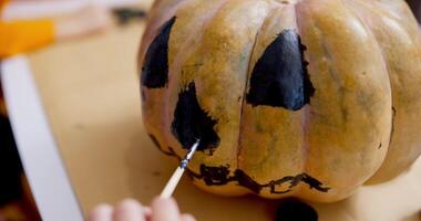 Close-up of a hand painting a jack-o'-lantern face on a pumpkin with black paint video
