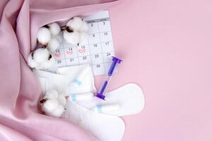 Women's menstrual pads, tampons, female menstruation calendar and alarm clock on a pink background. photo