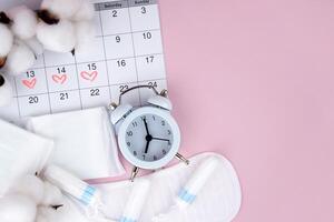 Women's menstrual pads, tampons, female menstruation calendar and alarm clock on a pink background. photo