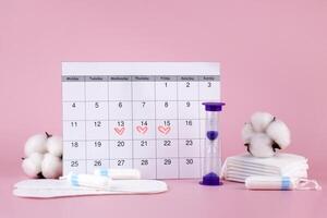 Women's menstrual pads, tampons, female menstruation calendar and alarm clock on a pink background. photo