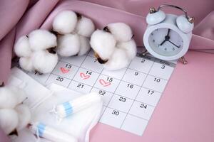 Women's menstrual pads, tampons, female menstruation calendar and alarm clock on a pink background. photo