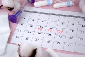 Women's menstrual pads, tampons, female menstruation calendar and alarm clock on a pink background. photo