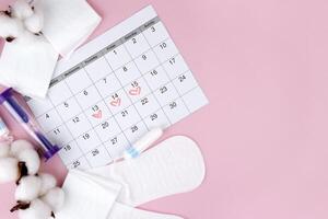 Women's menstrual pads, tampons, female menstruation calendar and alarm clock on a pink background. photo