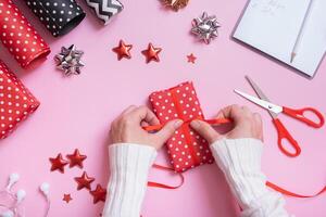 Female hands wrapping christmas presents flat lay on pink background. Top view xmas prepare photo