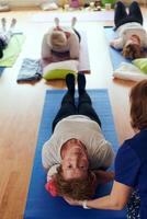 A group of senior women engage in various yoga exercises, including neck, back, and leg stretches, under the guidance of a trainer in a sunlit space, promoting well-being and harmony photo