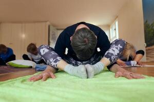 A group of senior women engage in various yoga exercises, including neck, back, and leg stretches, under the guidance of a trainer in a sunlit space, promoting well-being and harmony photo