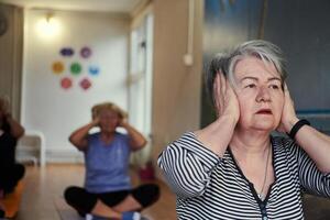 A group of senior women engage in various yoga exercises, including neck, back, and leg stretches, under the guidance of a trainer in a sunlit space, promoting well-being and harmony photo