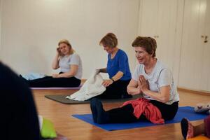 A group of senior women engage in various yoga exercises, including neck, back, and leg stretches, under the guidance of a trainer in a sunlit space, promoting well-being and harmony photo