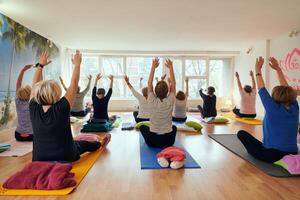 A group of senior women engage in various yoga exercises, including neck, back, and leg stretches, under the guidance of a trainer in a sunlit space, promoting well-being and harmony photo