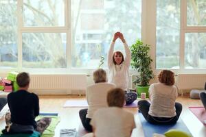 A group of senior women engage in various yoga exercises, including neck, back, and leg stretches, under the guidance of a trainer in a sunlit space, promoting well-being and harmony photo