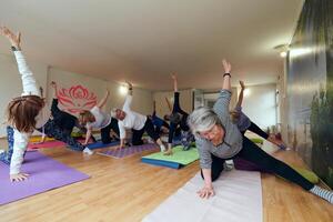 A group of senior women engage in various yoga exercises, including neck, back, and leg stretches, under the guidance of a trainer in a sunlit space, promoting well-being and harmony photo