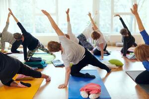 A group of senior women engage in various yoga exercises, including neck, back, and leg stretches, under the guidance of a trainer in a sunlit space, promoting well-being and harmony photo