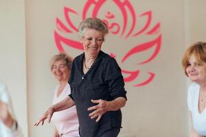 A group of senior women engage in various yoga exercises, including neck, back, and leg stretches, under the guidance of a trainer in a sunlit space, promoting well-being and harmony photo