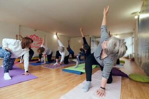 A group of senior women engage in various yoga exercises, including neck, back, and leg stretches, under the guidance of a trainer in a sunlit space, promoting well-being and harmony photo