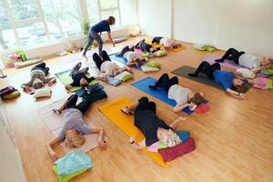 A group of senior women engage in various yoga exercises, including neck, back, and leg stretches, under the guidance of a trainer in a sunlit space, promoting well-being and harmony photo